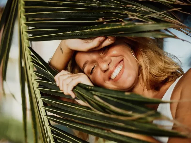 Happy woman, peeking out through a palm tree because she healed her digestive issues.