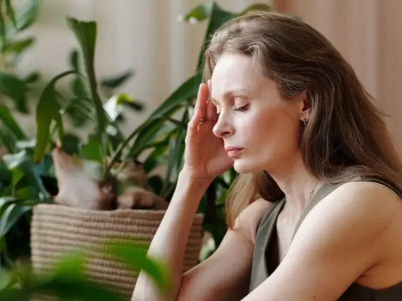 Woman with thyroid issues with her hand to her head and eyes closed.